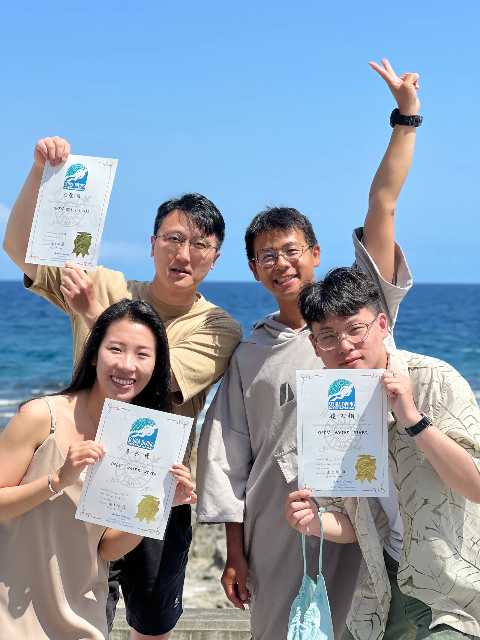 教練與學員在海邊手持開放水域潛水員證書合照